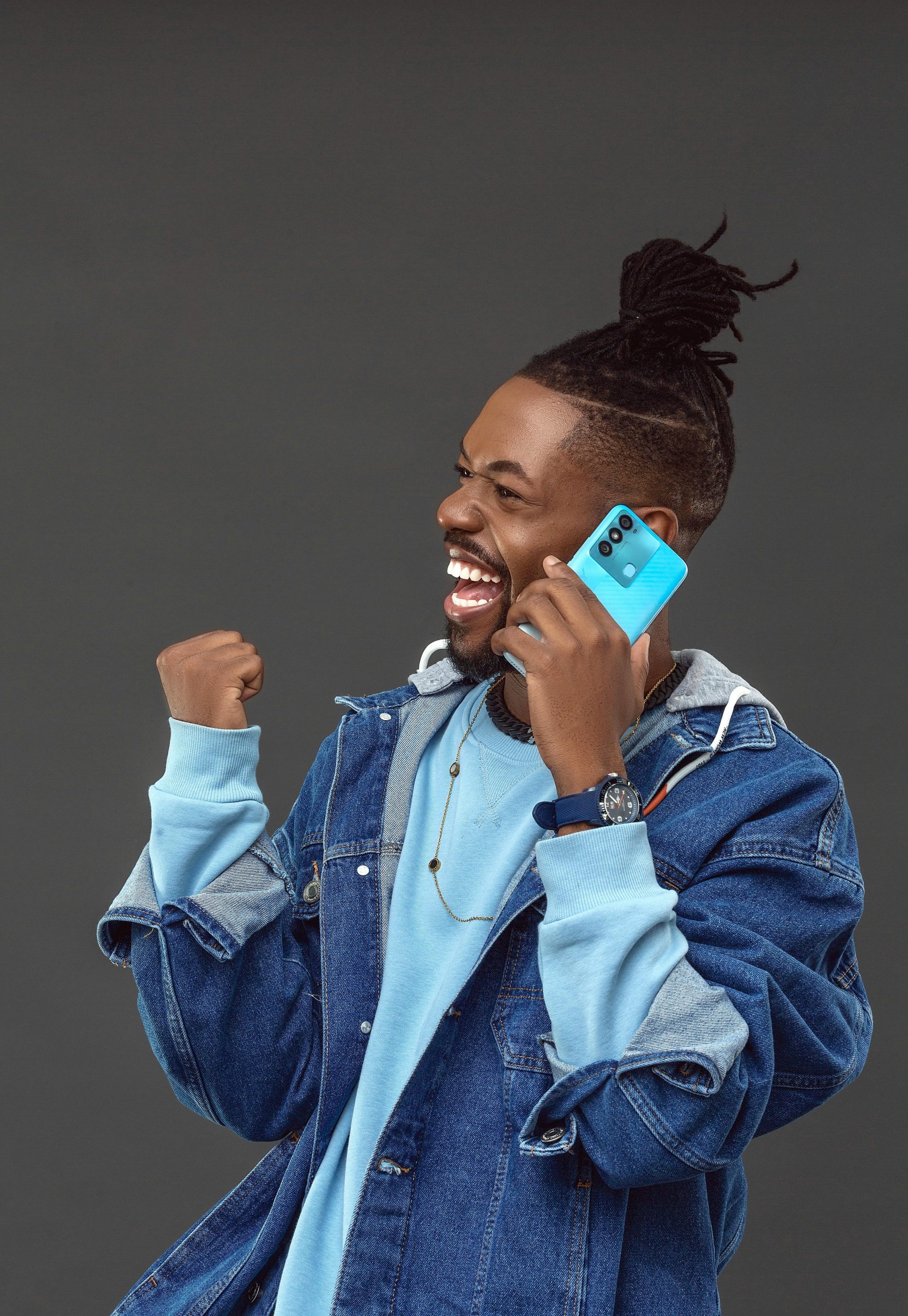 A happy African American man celebrates while talking on his smartphone, wearing a stylish denim jacket.