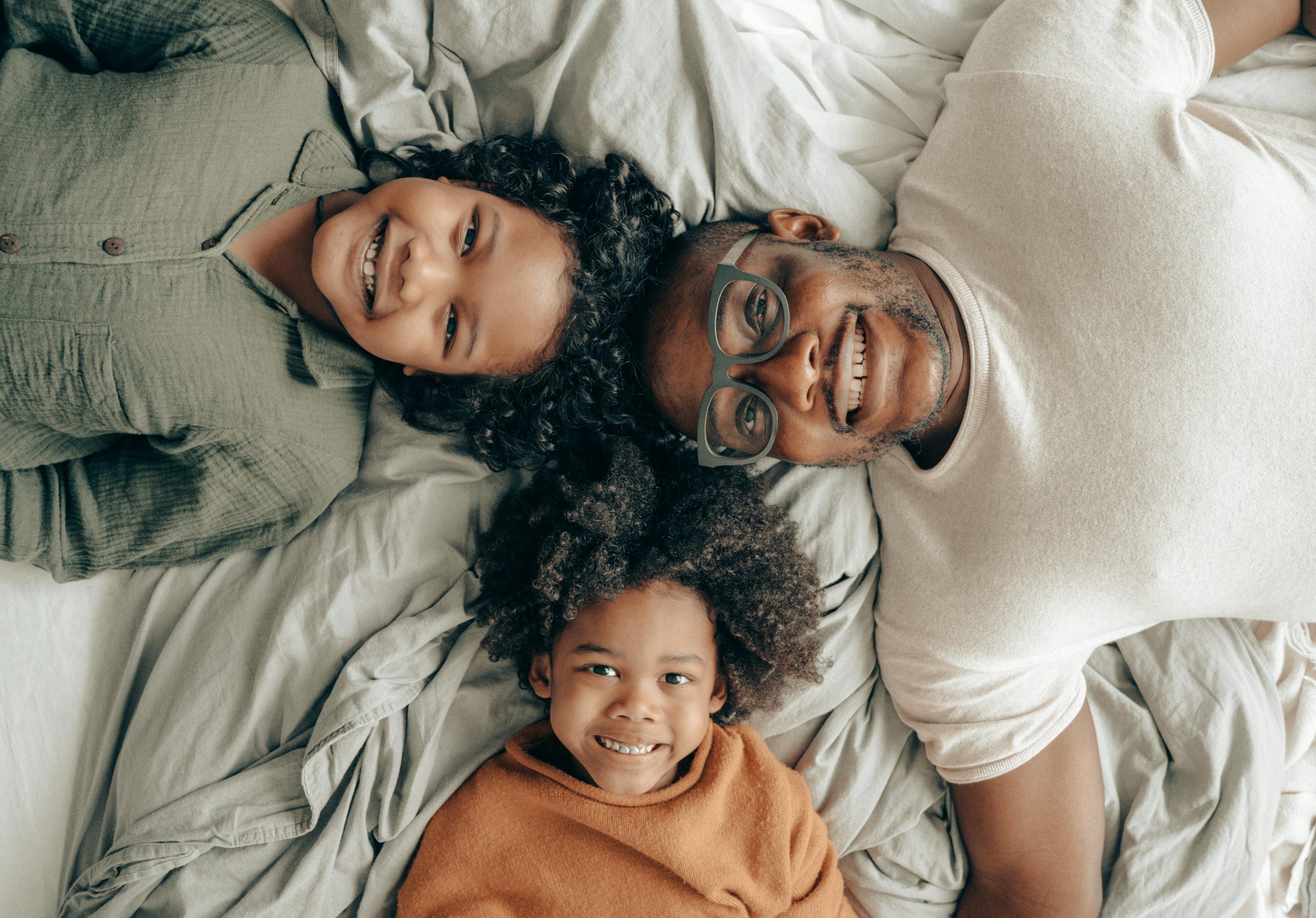 Joyful family of a father with his children enjoying a cozy moment on a bed, smiling warmly.