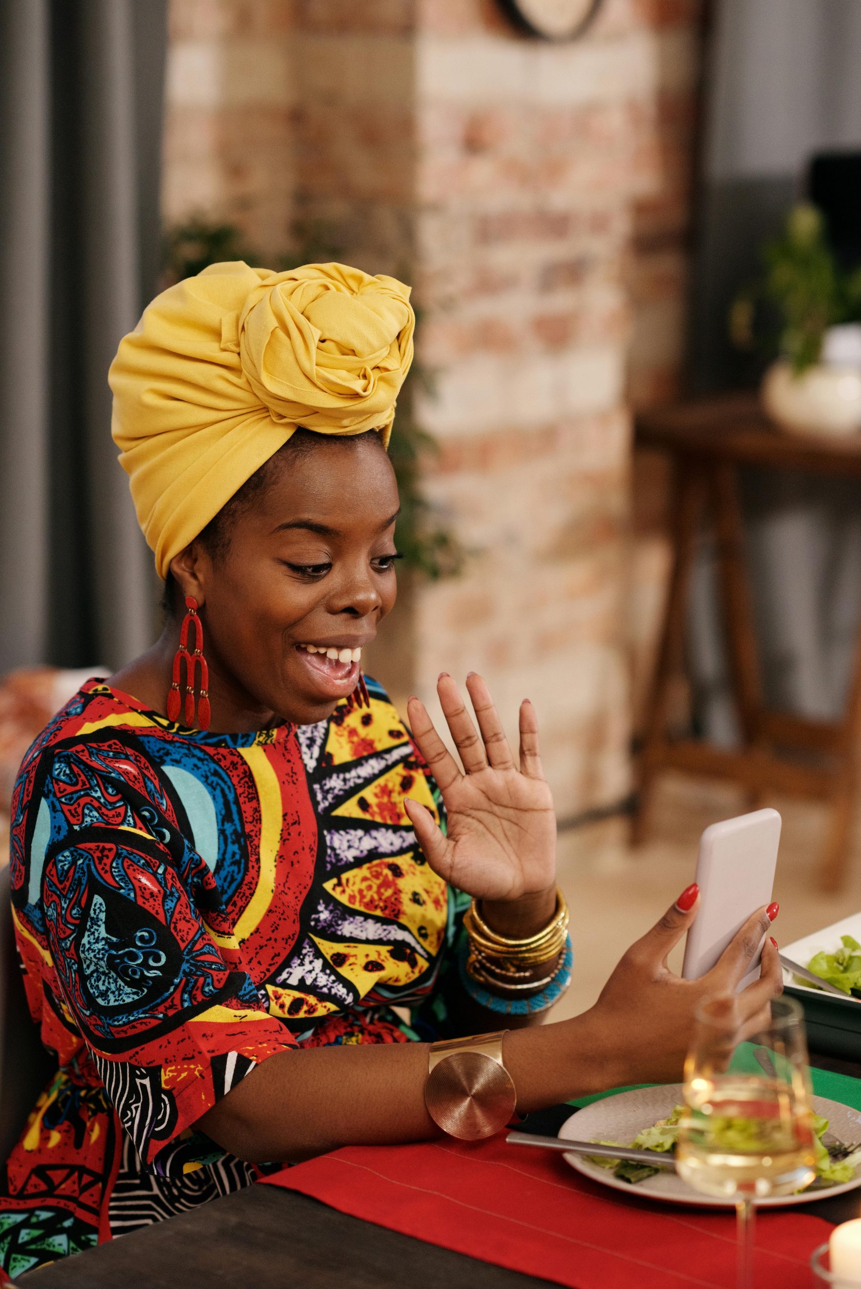 A joyful woman in vibrant attire video calling, celebrating indoors.