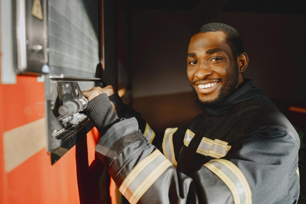 Professional firefighter standing in uniform smiling beside a fire truck.