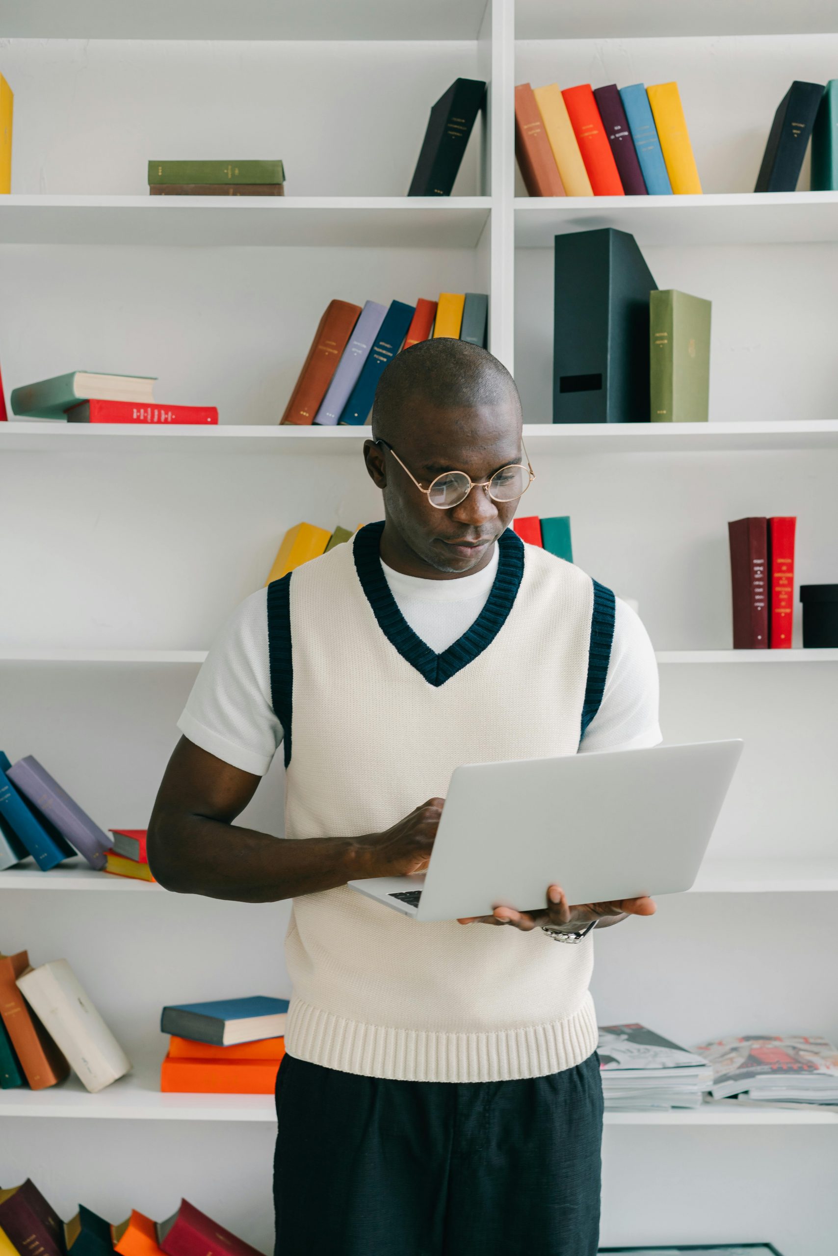 Focused teacher using laptop in a bright modern library, surrounded by colorful books.