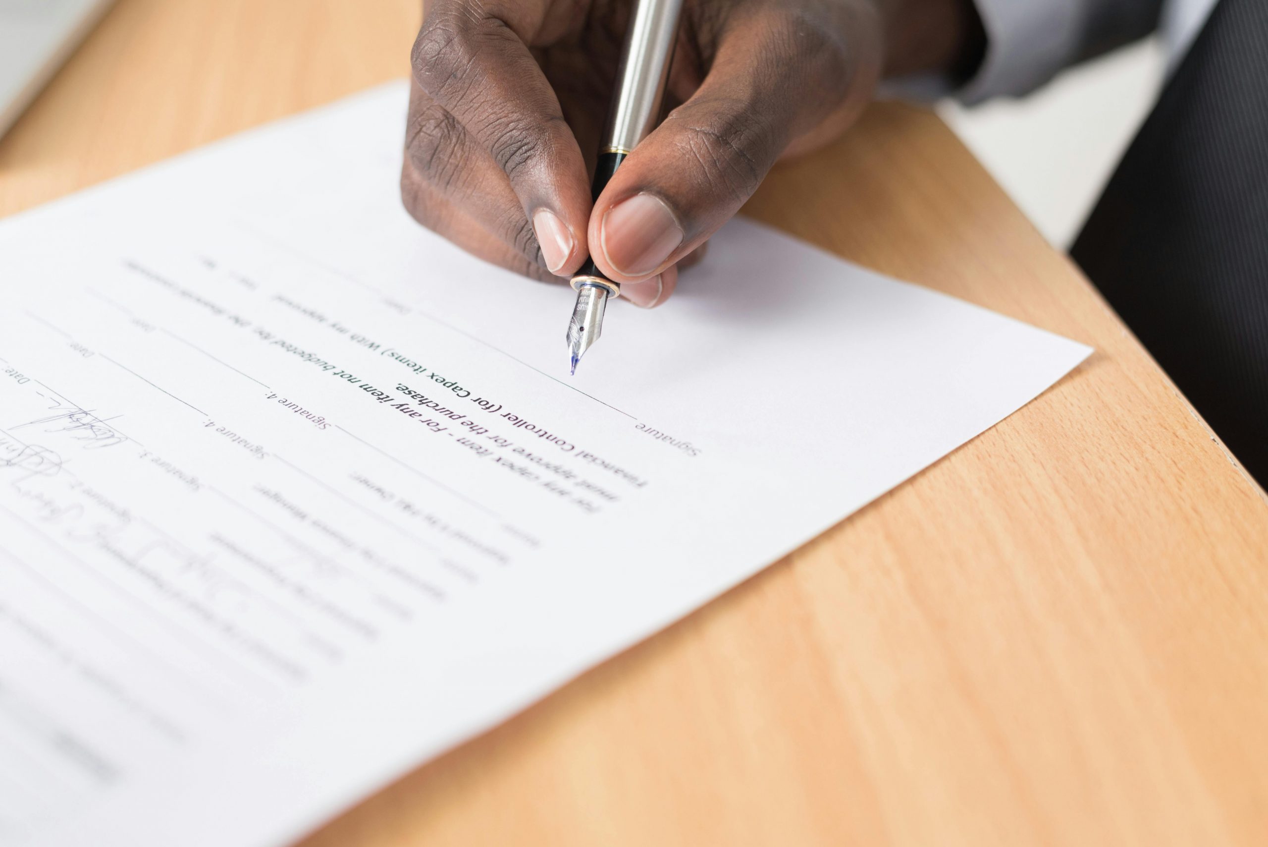 A hand holding a pen signing a document close-up on a desk, symbolizing agreement or contract finalization.