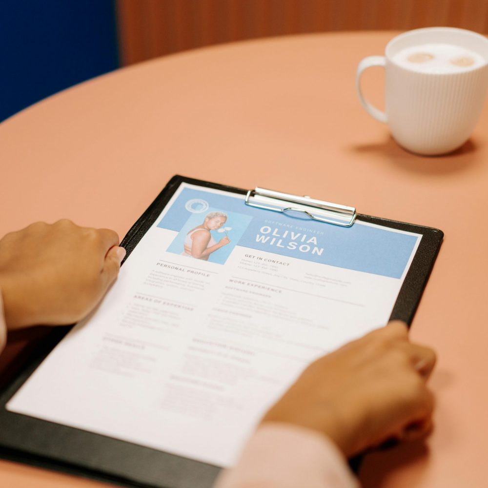 Close-up of hands holding resume during interview with coffee on table, highlighting workplace setting.