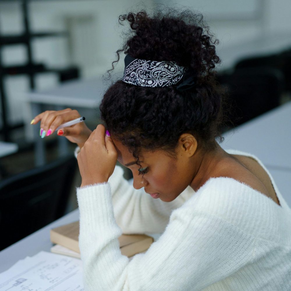 A young woman deeply concentrating while sitting at a desk with study materials.