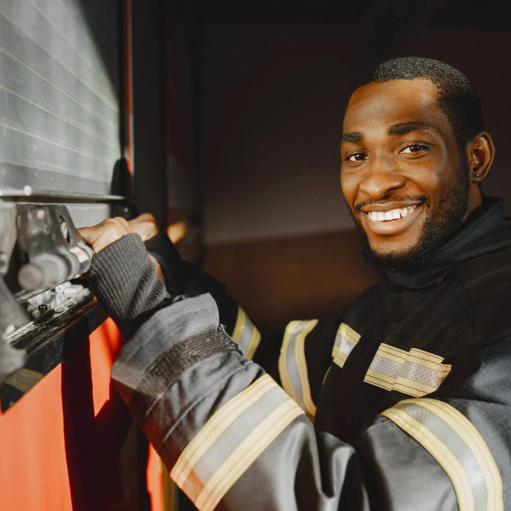 Professional firefighter standing in uniform smiling beside a fire truck.